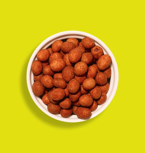 Brass bowl of roasted peanuts coated in a reddish masala, the style of snack in a Balaji Katak Batak pack.